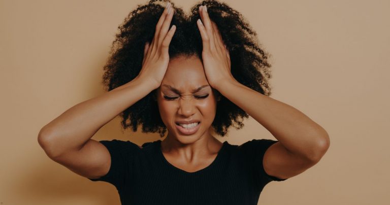 A Black woman holding her hands up to her forehead, making a face as if in pain. It looks like she's experiencing a migraine.